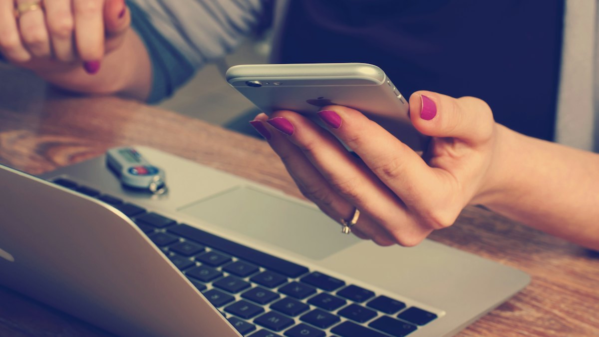 Personne consultant son téléphone devant un ordinateur portable